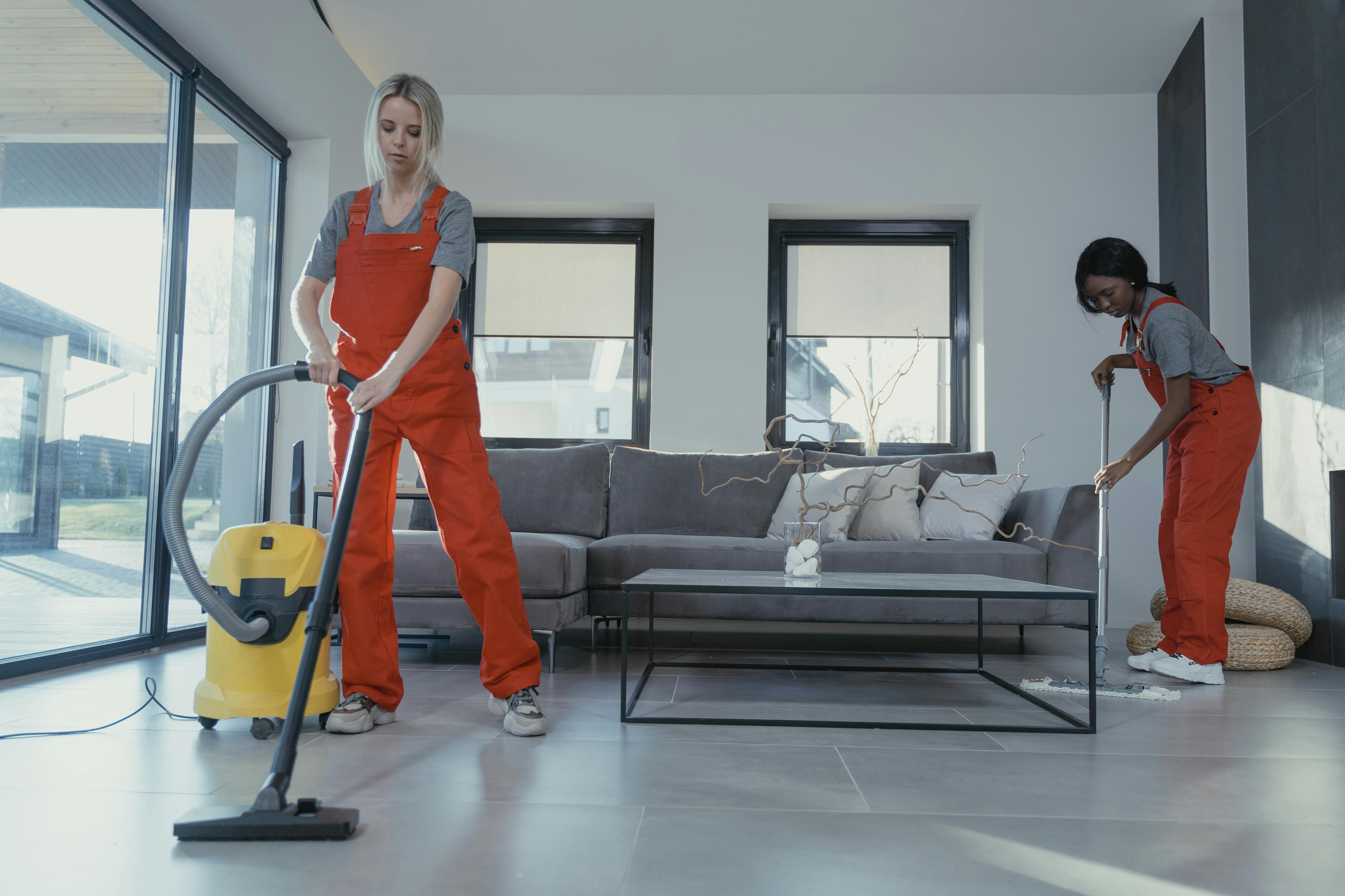 Two professional cleaners vacuuming and mopping in a modern living room